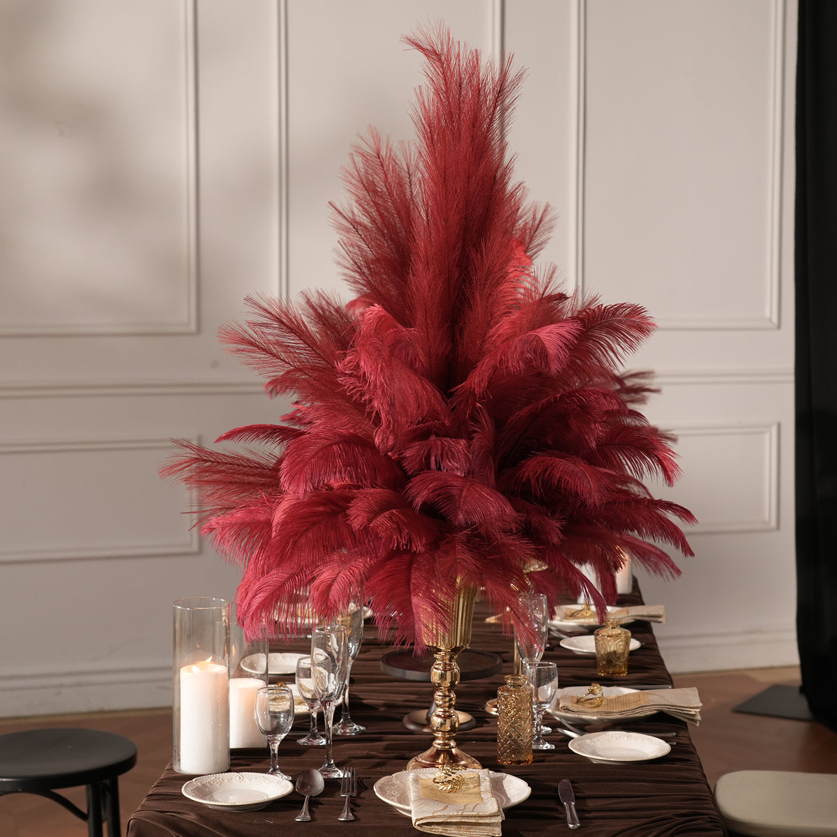 Burgundy ostrich feather plumes arranged inside gold pedestal vase
