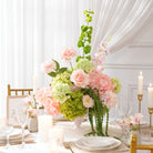 Long wedding dinner table lined with soft pink‑green faux floral centerpieces