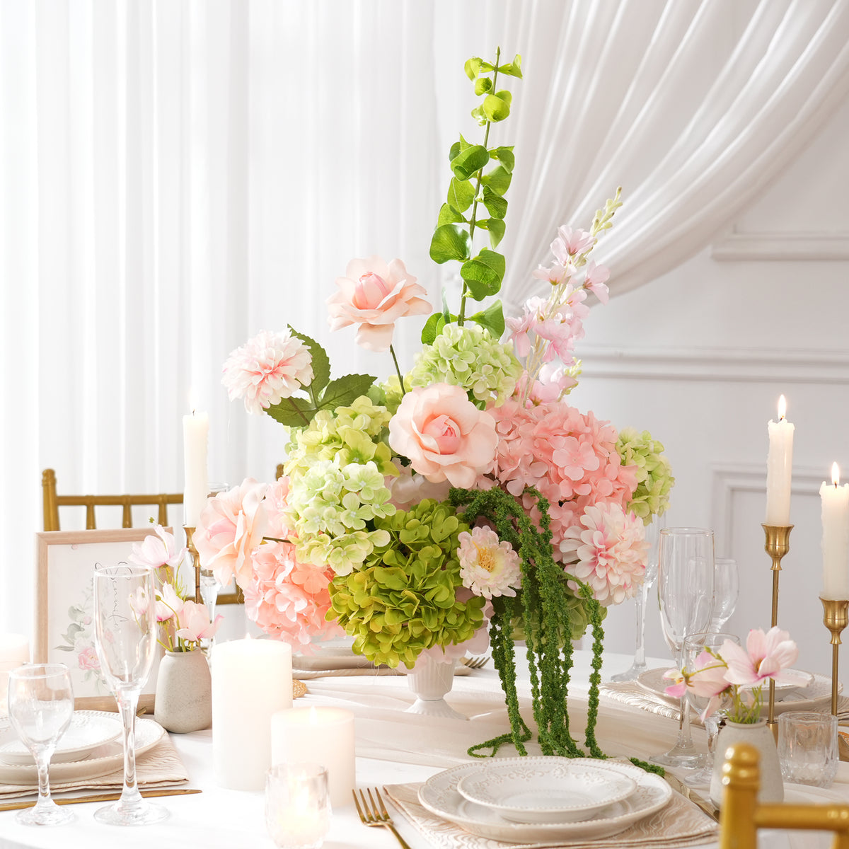 Long wedding dinner table lined with soft pink‑green faux floral centerpieces