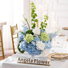 Long wedding dinner table decorated with soft blue‑white faux floral vase arrangements