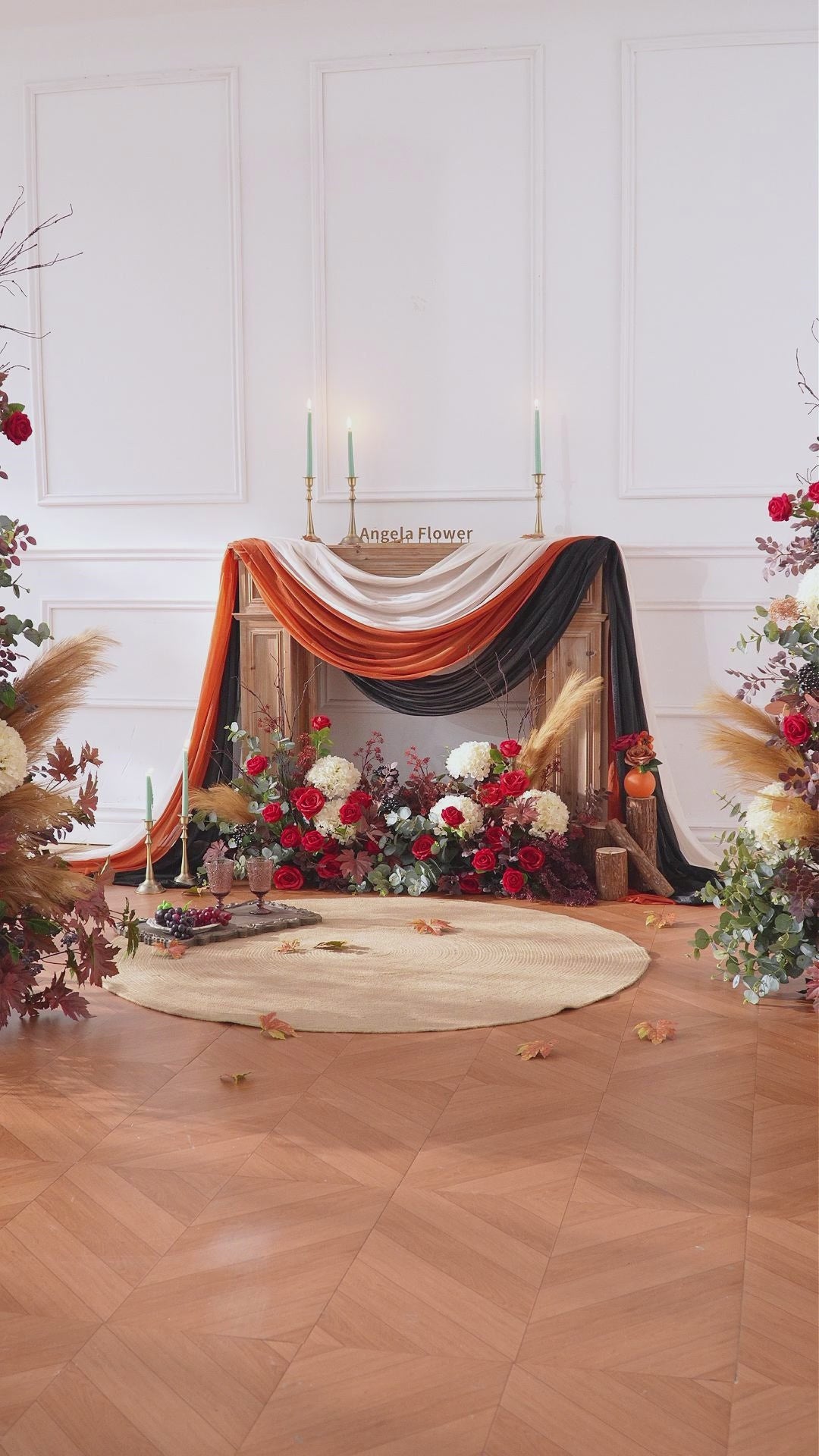 Barn‑style wedding ceremony KT panel with flowing wine‑red silk drapes and autumn artificial blooms