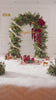 Outdoor holiday arch installation with faux winter greenery and deep red magnolia blooms