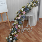Tablescape with cascading artificial flower runner on white tablecloth for wedding banquet setup